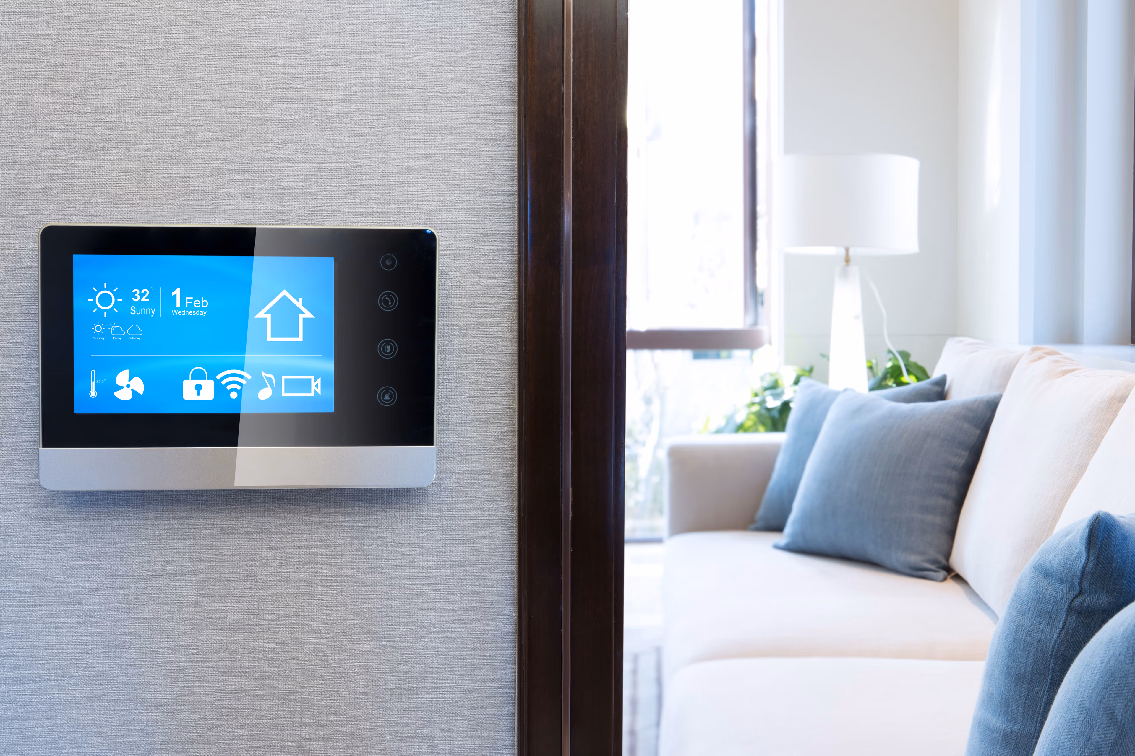 A modern, touch-screen home automation control panel mounted on a wall, with various icons and controls displayed on the screen, set against a cozy living room environment with a comfortable sofa and decor.